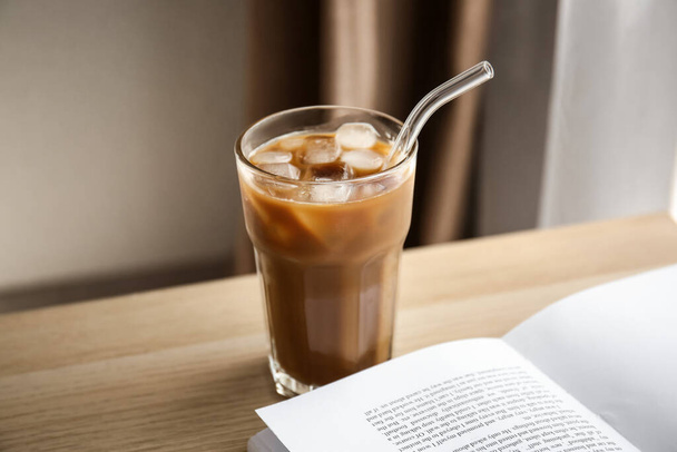 Sklenice chutné ledové kávy s mlékem a knihou na dřevěném stole - Fotografie, Obrázek