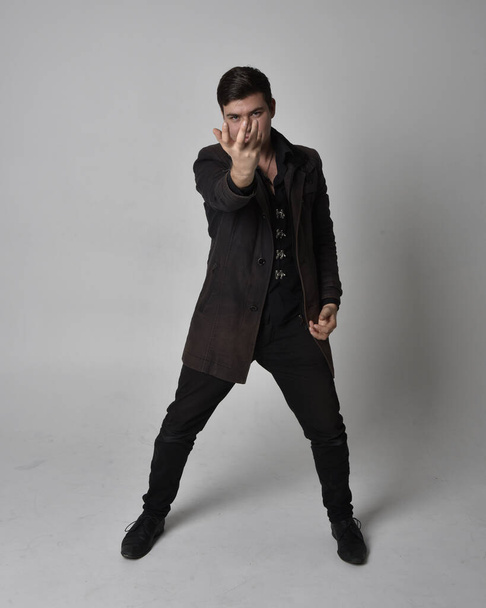 Full length portrait of a brunette man wearing black leather coat.  Standing pose  isolated  against a grey studio background. - Foto, Bild
