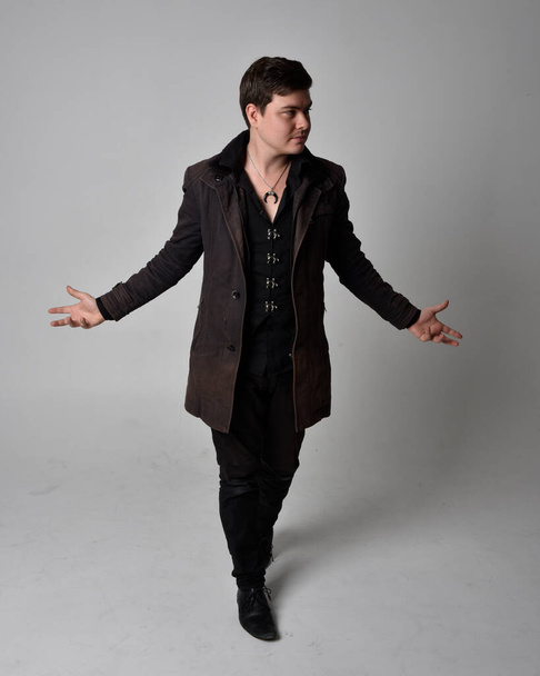 Full length portrait of a brunette man wearing black leather coat.  Standing pose  isolated  against a grey studio background. - Фото, зображення