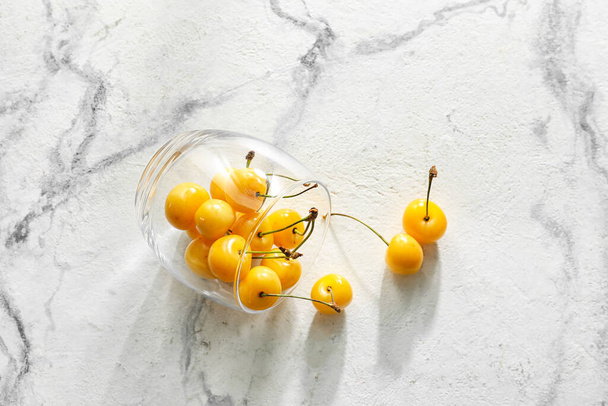 Glass with tasty sweet cherries on light background - 写真・画像