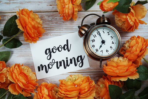 Good Morning card and alarm clock with orange flower decoration on wooden background - Valokuva, kuva