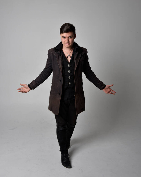 Full length portrait of a brunette man wearing black leather coat.  Standing pose  isolated  against a grey studio background. - Fotografie, Obrázek