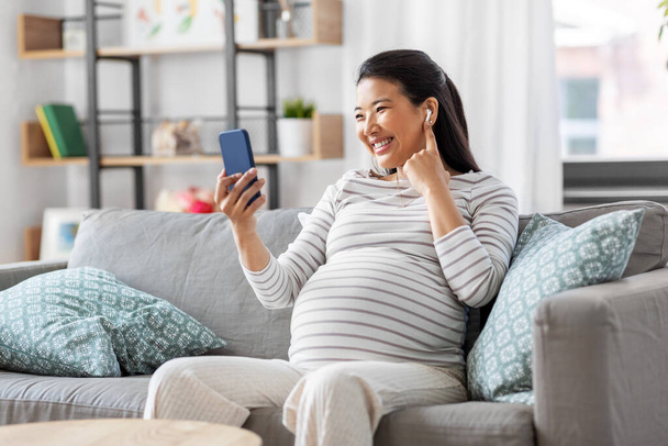 pregnant woman with phone and earphones at home - Foto, Bild