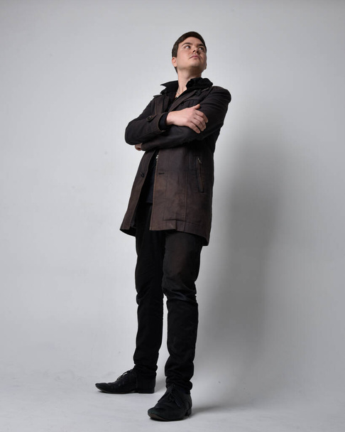 Siyah deri ceket giyen esmer bir adamın tam boy portresi. Gri bir stüdyonun arka planında izole bir şekilde duruyor.. - Fotoğraf, Görsel