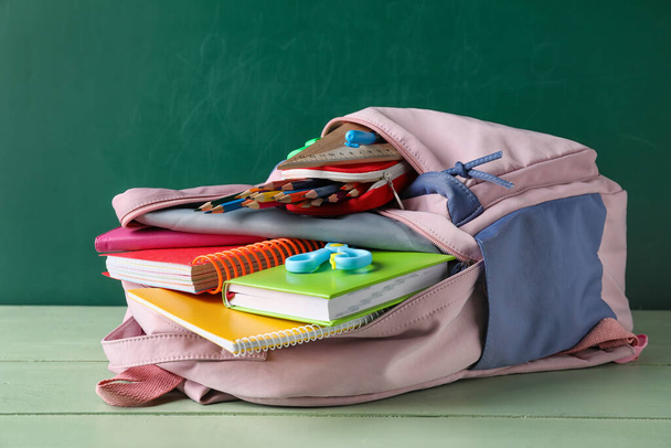 School backpack and stationery on table near blackboard - Foto, afbeelding