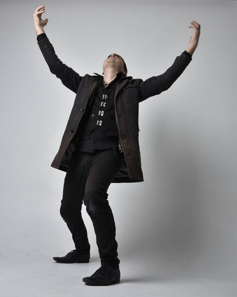 Retrato de comprimento total de um homem morena usando casaco de couro preto. pose de pé isolado contra um fundo estúdio cinza. - Foto, Imagem