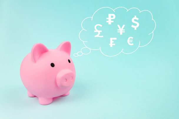 Pink piggy bank with digital hologram world currencies in cloud thought above his head on blue background. Money saving for future investment and retirement concept - Fotoğraf, Görsel