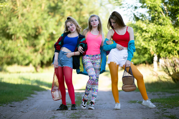 Tres hermosas chicas del campo vestidas al estilo de los noventa están caminando por el camino. - Foto, imagen