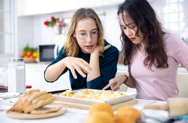 Όμορφη αρτοποιός κάνει γλυκά, Χαριτωμένο ευτυχισμένη δύο γυναίκες διασκεδάζουν ένα ψωμί κάνοντας τάξη και χρησιμοποιούν τα χέρια τους για να χαστουκίσει τη ζύμη μαζί για να κάνουν κέικ μαζί στην κουζίνα του σπιτιού. - Φωτογραφία, εικόνα