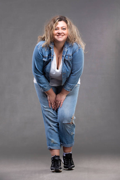 Красивая пухлая женщина в джинсовом костюме на сером фоне. - Фото, изображение