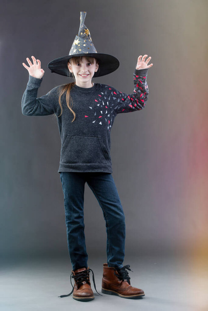 魔女の帽子の少女は灰色の背景にいる。ハロウィンの祭りの子. - 写真・画像