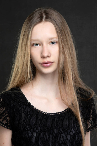 Beautiful teenager girl with long hair on a gray background. A girl with a European face type. - Foto, afbeelding