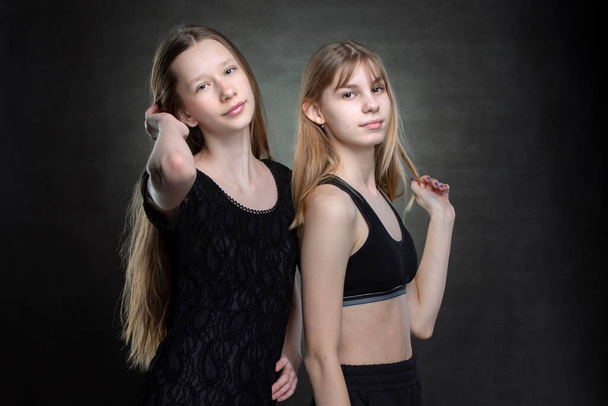 Two beautiful teenage girls on a dark background are looking at the camera. - Photo, Image