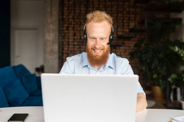 Portrait of cheerful red haired hipster guy in wireless headset - Фото, изображение