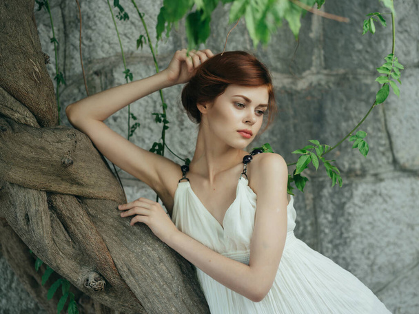 Yunanistan 'ın ağaç tabanlı taş duvarının yanındaki beyaz elbiseli kadın. - Fotoğraf, Görsel