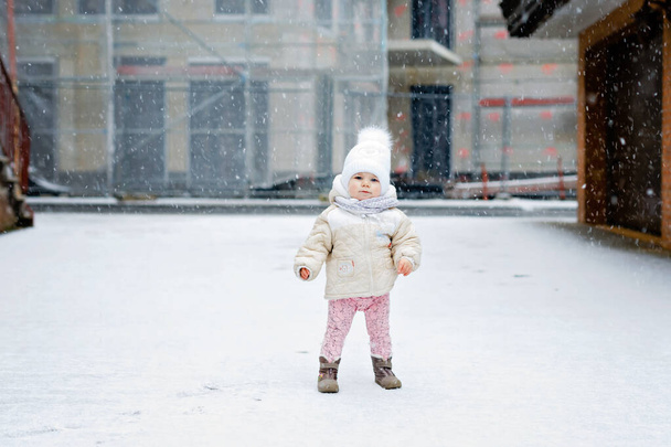 Bonne petite fille qui fait ses premiers pas à l'extérieur en hiver à travers la neige. Bébé mignon apprenant à marcher. Enfant qui s'amuse par temps froid et neigeux. Bébés première neige, activité. Promenade hivernale en plein air - Photo, image