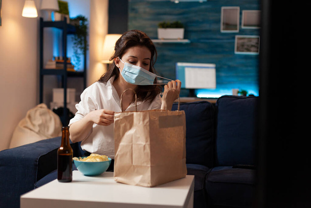 Cheerful woman taking medical protection face mask out after purchasing takeaway food - Photo, Image