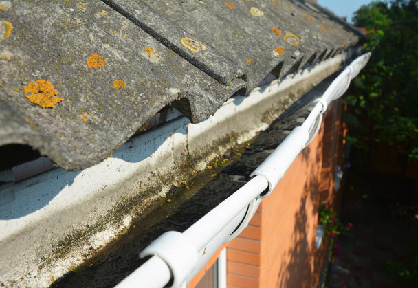 Roof gutter cleaning. A close-up of a dirty rain gutter that needs cleaning, full of dirt and debris attached to an old asbestos roof. - Photo, Image