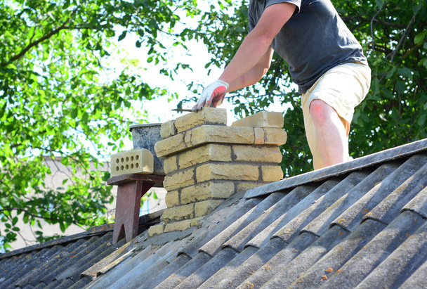 Construção e reconstrução de chaminés. Um empreiteiro está construindo uma chaminé em um telhado de amianto. - Foto, Imagem