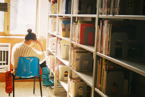 young woman sitting in library and reading book in the room - Фото, изображение