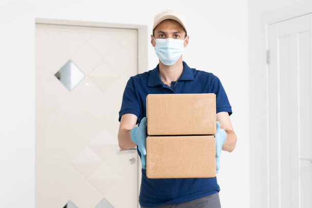 Man from delivery service in t-shirt, in protective mask and gloves giving food order and holding boxes over white background. - Zdjęcie, obraz
