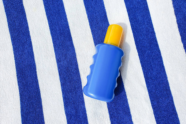 Frasco de spray cosmético azul y amarillo sin marca sobre toalla de playa a rayas. Vista superior, maqueta. Botella de protector solar. - Foto, Imagen