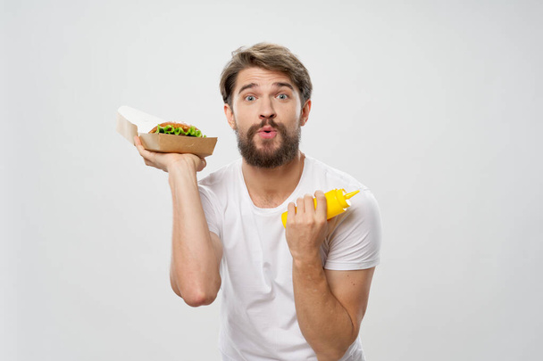 férfi fehér pólóban hamburger gyorskaját eszik - Fotó, kép