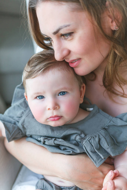 Uma bela jovem mãe com uma filhinha de olhos azuis está descansando em casa. - Foto, Imagem