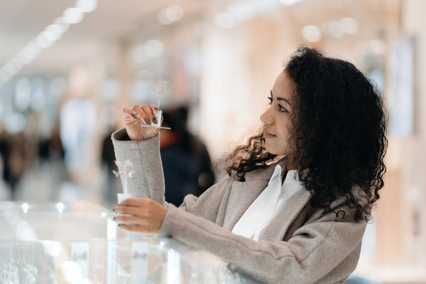молодая женщина выбирает серьги в ювелирном магазине. - Фото, изображение