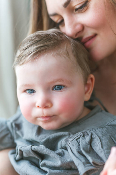 Una hermosa madre joven con una hijita de ojos azules descansa en casa. - Foto, Imagen