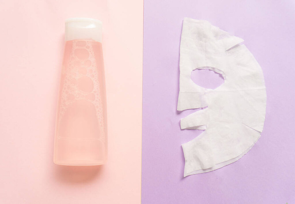 ピンクやライラックを背景にしたフェイスマスクとピンクの化粧水。創造的なコンセプト. - 写真・画像