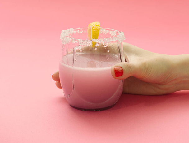 Rosafarbener Cocktail mit Zitronenscheibe und Salz in der Hand der Frau auf rosa Hintergrund. Kreatives Konzept. - Foto, Bild