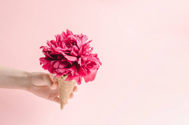 Copa de oblea para helado con una flor de peonía en la mano de una mujer. Concepto de regalos de verano y verano - Foto, Imagen
