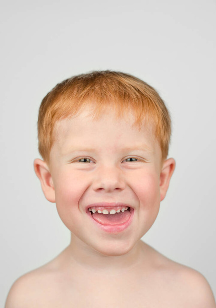 4 yaşındaki kızıl saçlı çocuğun yakın portresi. Çocuk kameraya baktı ve gri bir arka planda güldü. Mutlu çocuk - Fotoğraf, Görsel