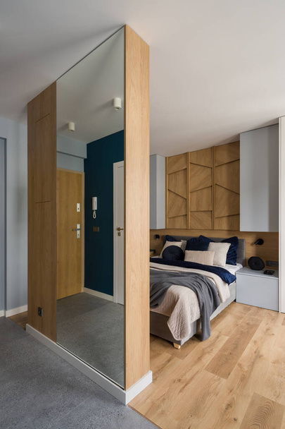 Elegante dormitorio con cama grande y cómoda con ropa de cama decorativa detrás de la pared de madera con espejo - Foto, imagen