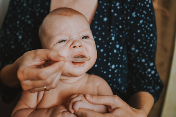 Matka i noworodek zabawny emocjonalny płacz niemowlę nagi chłopiec bierze płynne leki lub syrop przeciwgorączkowy medycyny z łyżki. Zdrowe dziecko, koncepcja szpitala i szczęśliwe macierzyństwo. Przedszkole. - Zdjęcie, obraz