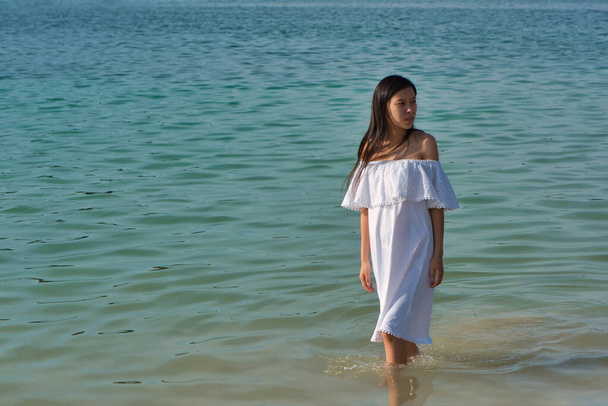Young asian pregnant woman in a white sundress in the water by the sea - Photo, Image