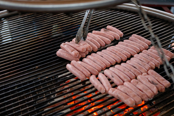 Chef grilling fresh meat sausages on big round hanging grill - close up - Photo, Image