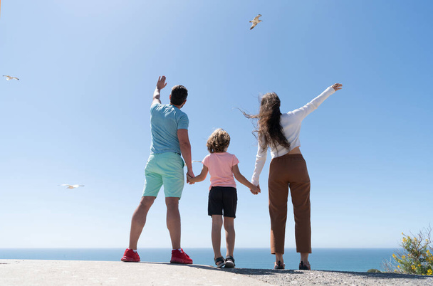 сім'я мати тато і дитина хлопчик дивиться в майбутньому тримає руки влітку, вид ззаду, благодійність
 - Фото, зображення