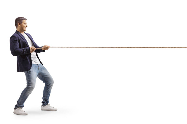 Full length profil záběr mladého ležérní muž tahání lano izolované na bílém pozadí - Fotografie, Obrázek