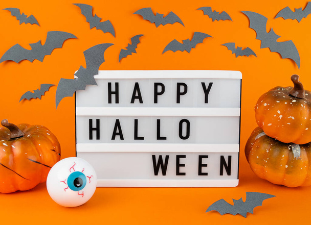 Caja de luz con feliz frase de Halloween con calabazas, murciélagos y decoración del globo ocular sobre un fondo naranja. - Foto, Imagen