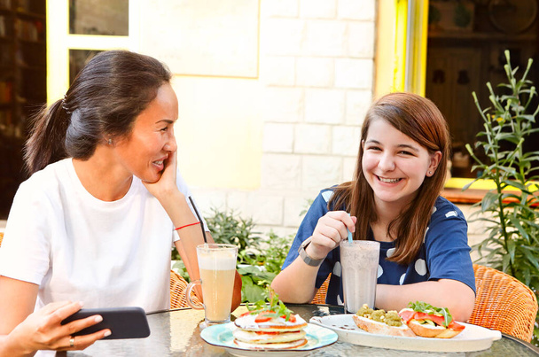 Szczęśliwy młody wielorasowe dziewczyny przyjaciele siedzi przy stole z kanapki i zimne napoje na tarasie kawiarni w porze lunchu - Zdjęcie, obraz