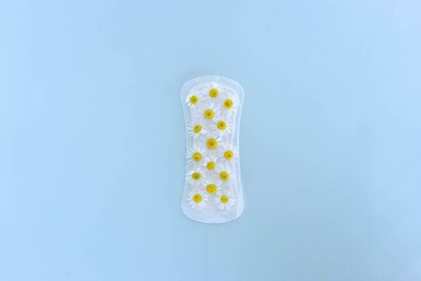 A sanitary pad with chamomile flowers on it lies on a yellow background. Menstruation days. Hygiene and freshness concept - Zdjęcie, obraz