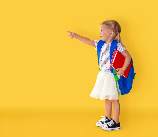 Back to school. Happy smiling girl with pointing finger at yellow background. - Valokuva, kuva
