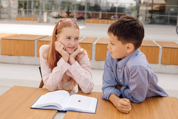 İlkokul, okul, arkadaşlık kavramı. Sırt çantalı iki genç kız ve erkek öğrenci okuldan sonra kitapla sohbet ediyorlar. - Fotoğraf, Görsel