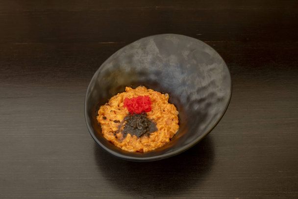 Bol noir avec tartare de pétoncles succulent avec oeufs de poisson rouge, sauce à la truffe et table en bois foncé - Photo, image