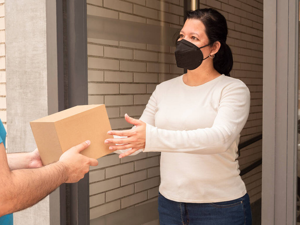 Белая женщина получает посылку в форме коробки без этикеток от курьера или почтальона у двери на улице - Фото, изображение