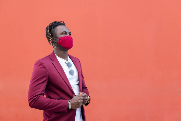 elegant african man with protective mask to match his suit on a red background, copy space for text, concept of elegance and fashionable lifestyle - Photo, Image