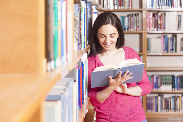 Portrait d'un jeune étudiant souriant lisant un livre dans une bibliothèque
 - Photo, image