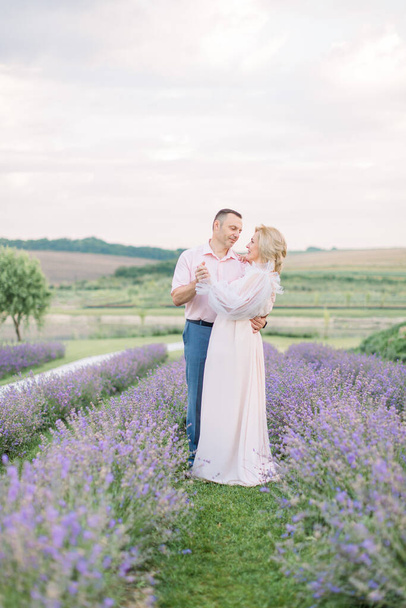 handsome man and elegant pretty blond lady, dating and walking together outdoor in lavender field - Фото, изображение